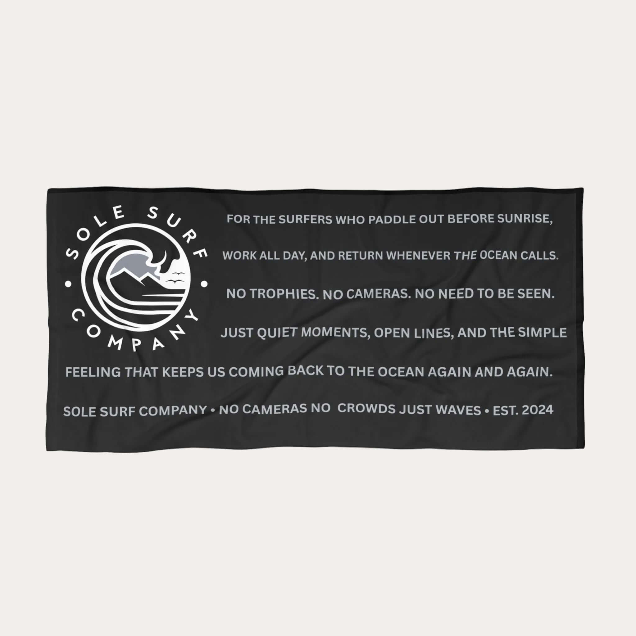 A black rectangular beach towel featuring white printed text and the Sole Surf Company logo, shown flat against a plain white background.
