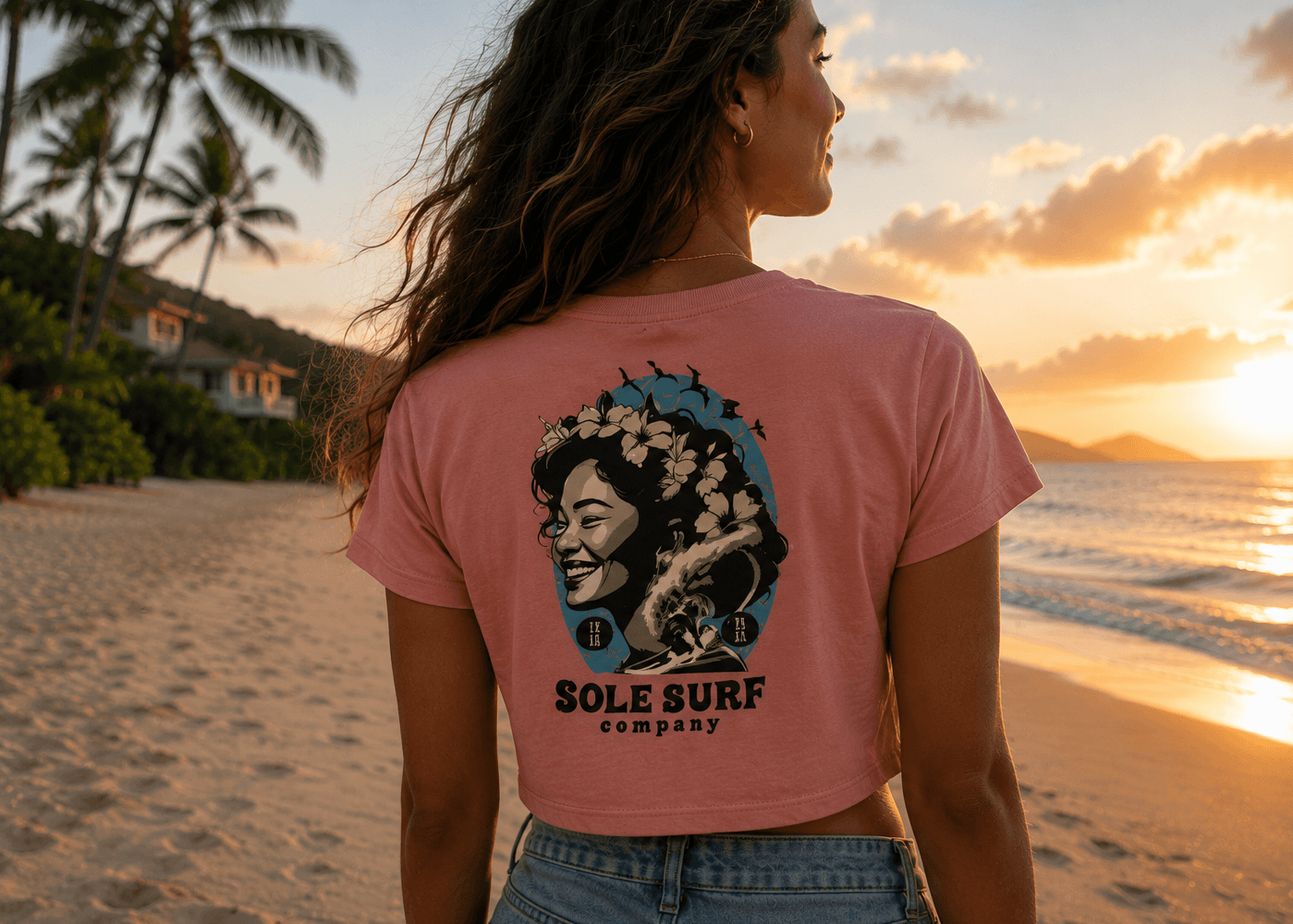 Woman wearing a pink t-shirt with 'Sole Surf Company' design on a beach at sunset.