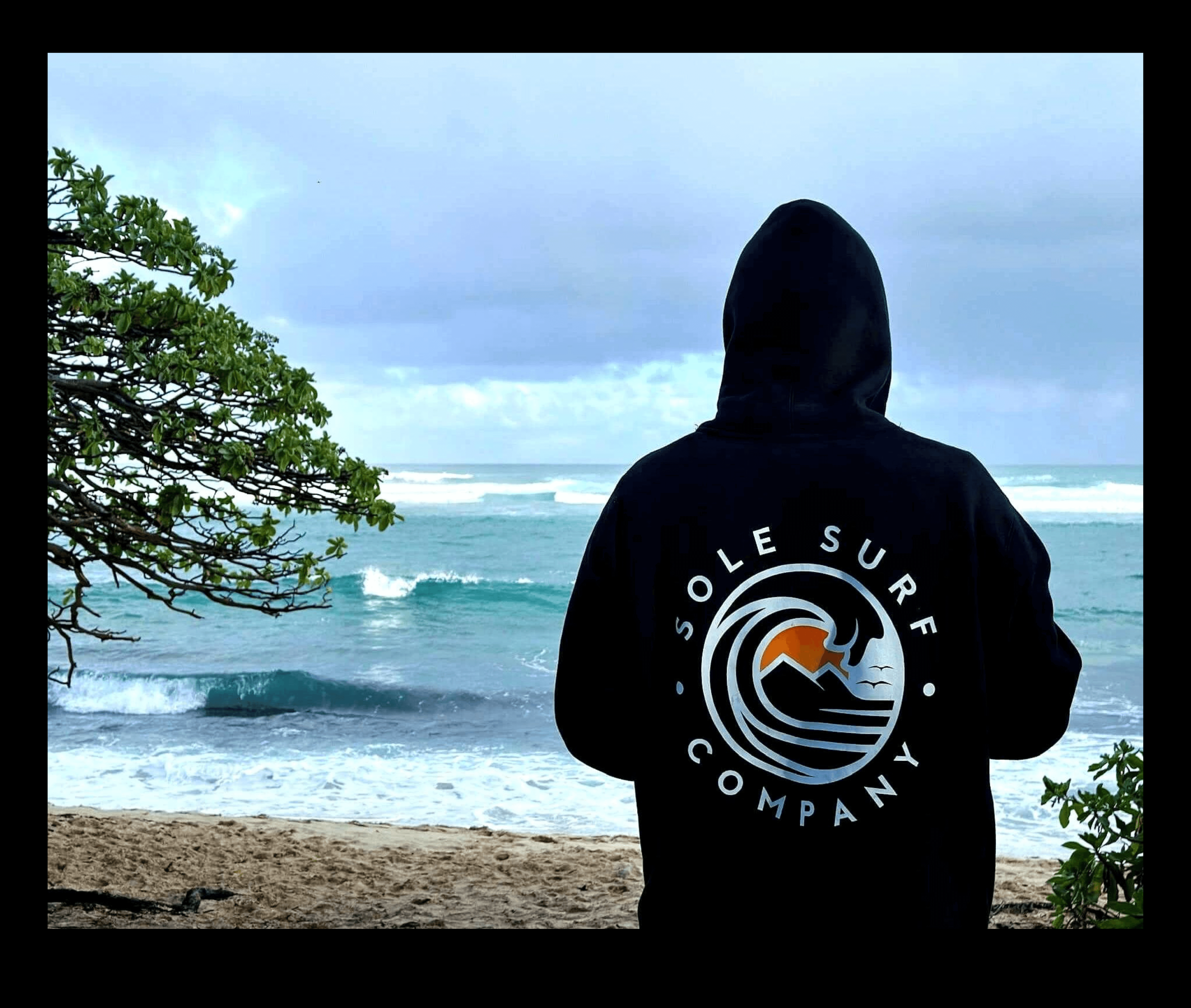 Man wearing Sole Surf Company hoodie by the beach, enjoying scenic ocean views.