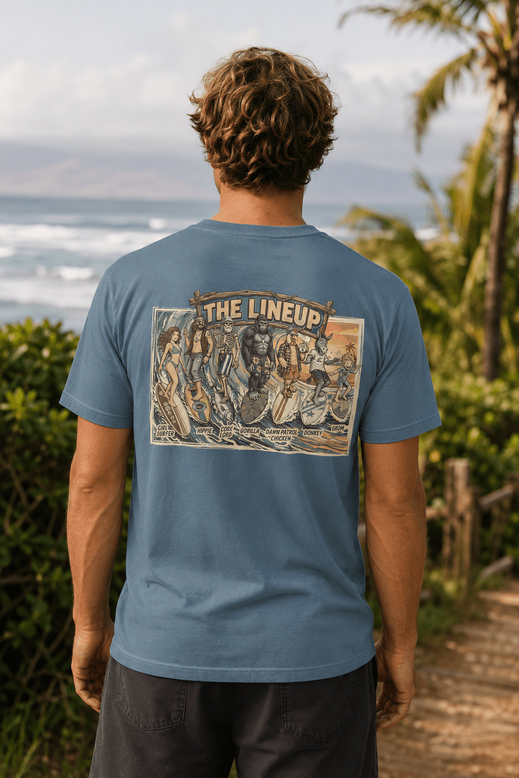 A man viewed from behind wearing a dusty blue t-shirt with a large vintage-style graphic print on the back that reads 'THE LINEUP'. The background shows a tropical beach scene with palm trees and the ocean.