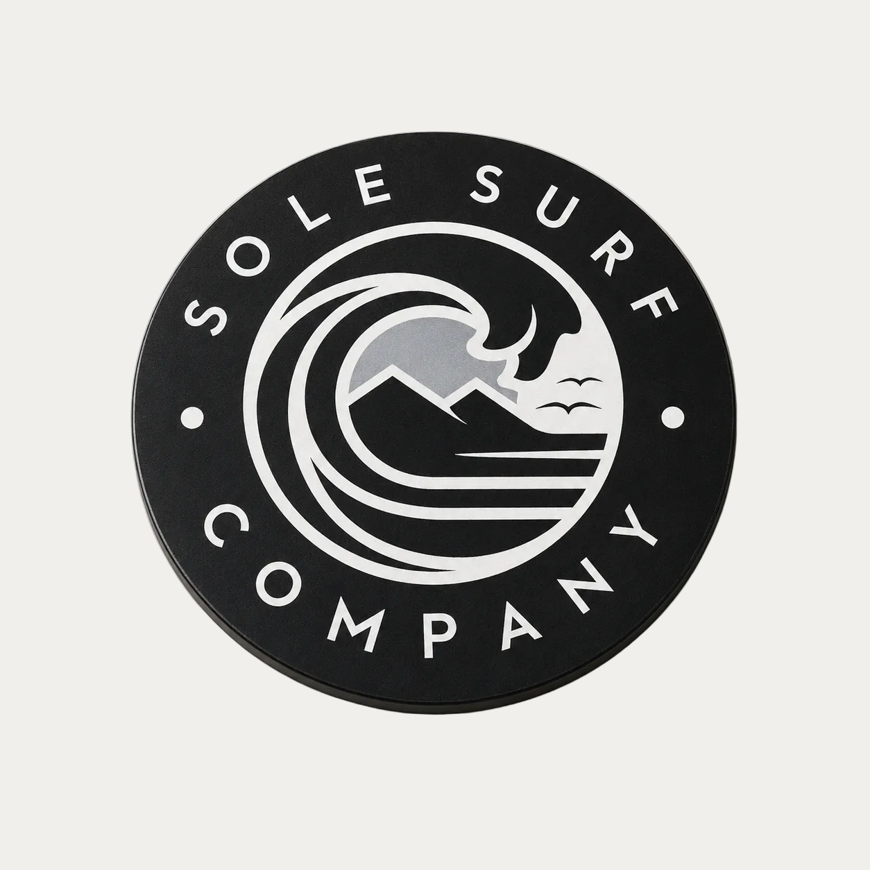 A circular black car magnet featuring the white 'Sole Surf Company' logo with a wave, mountains, and birds design, photographed on a light beige background.
