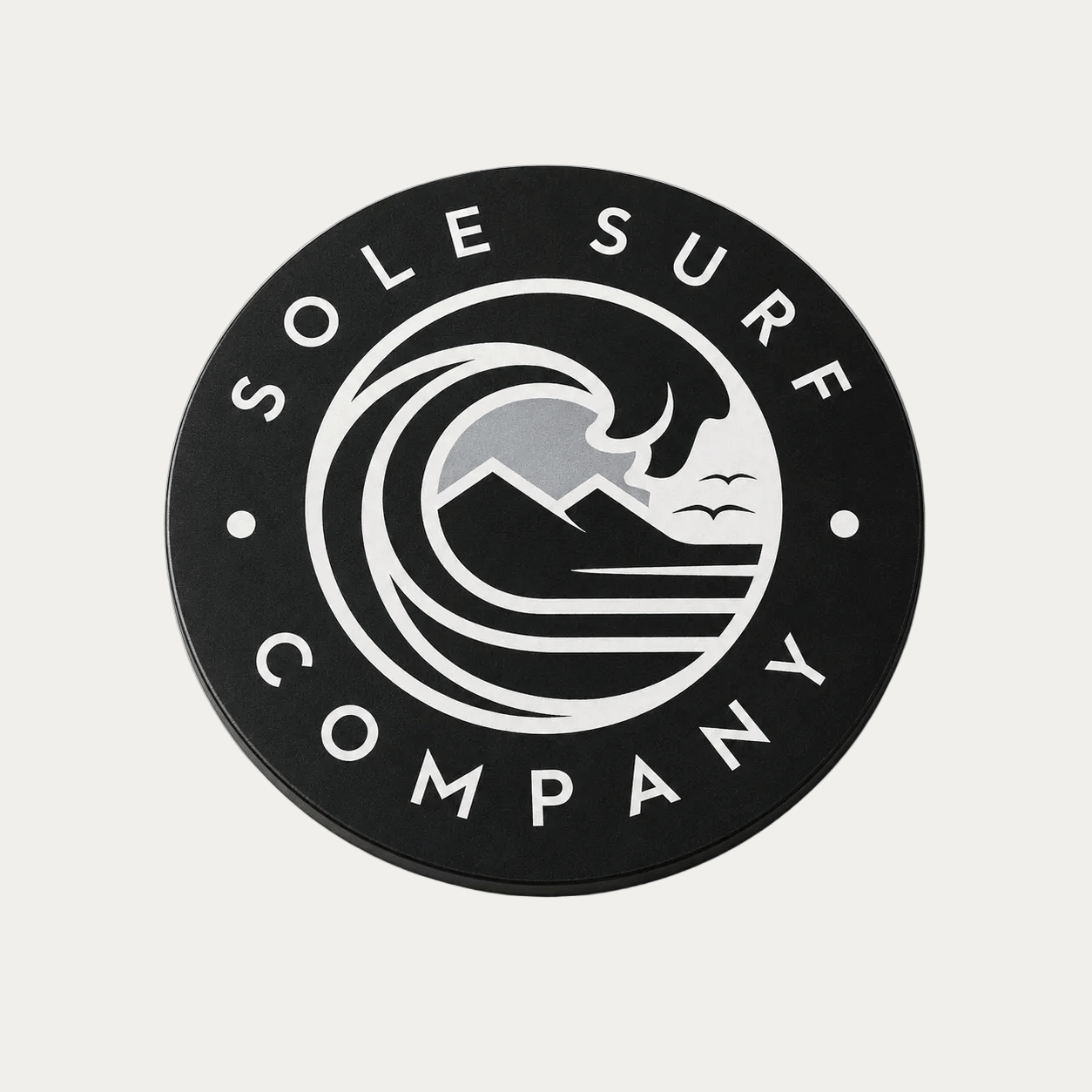 A circular black car magnet featuring the white 'Sole Surf Company' logo with a wave, mountains, and birds design, photographed on a light beige background.