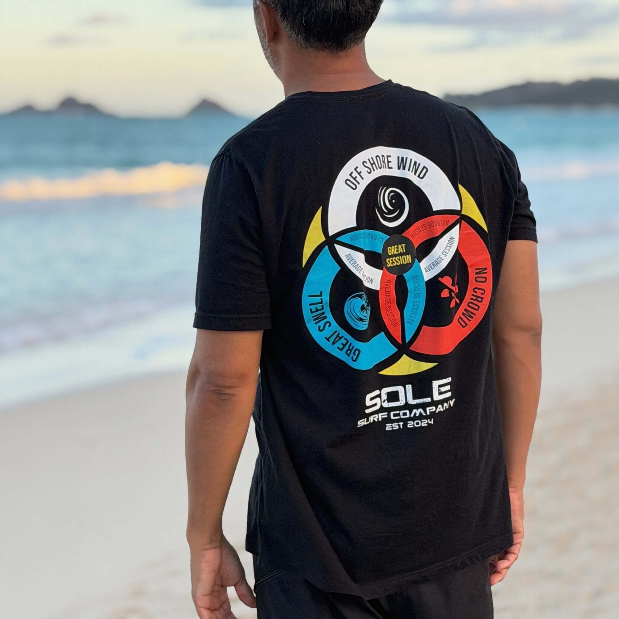 Person wearing a black t-shirt with a colorful graphic design on the beach