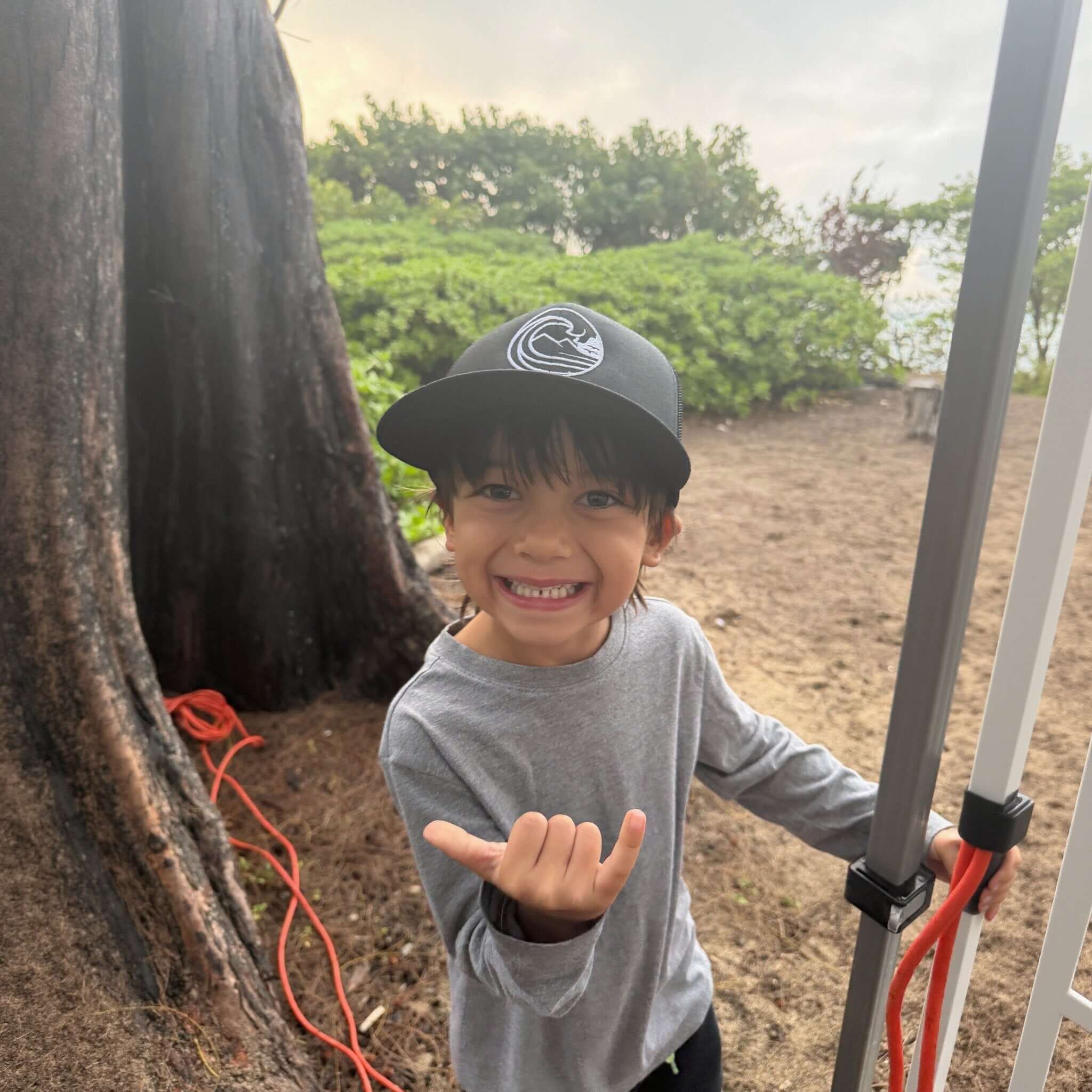 Smiling child wearing SSC Trucker Cap outdoors, showcasing a playful moment with the ocean in the background.
