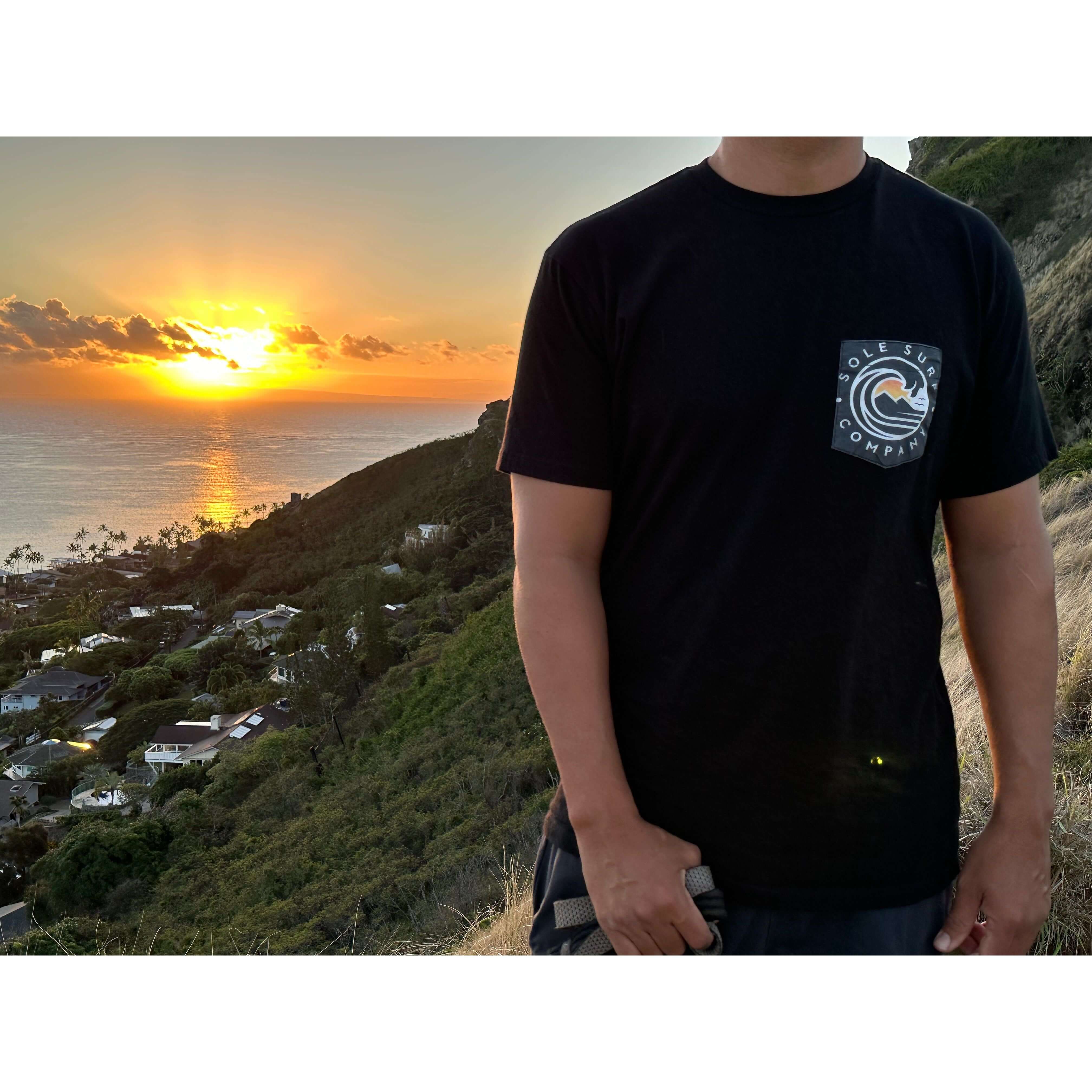 Black logo pocket tee worn during sunset, showcasing its premium fabric and casual style, ideal for beach outings.