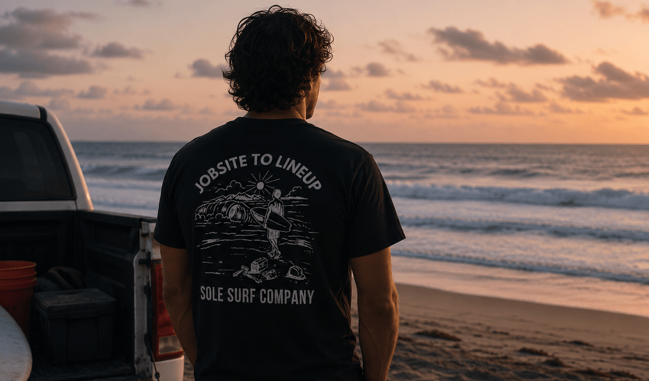 Person wearing a t-shirt with a graphic design standing on a beach at sunset.