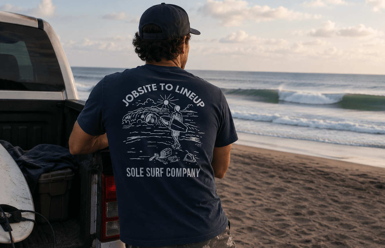 Person wearing a navy blue t-shirt with 'Sole Surf Company' logo on a beach