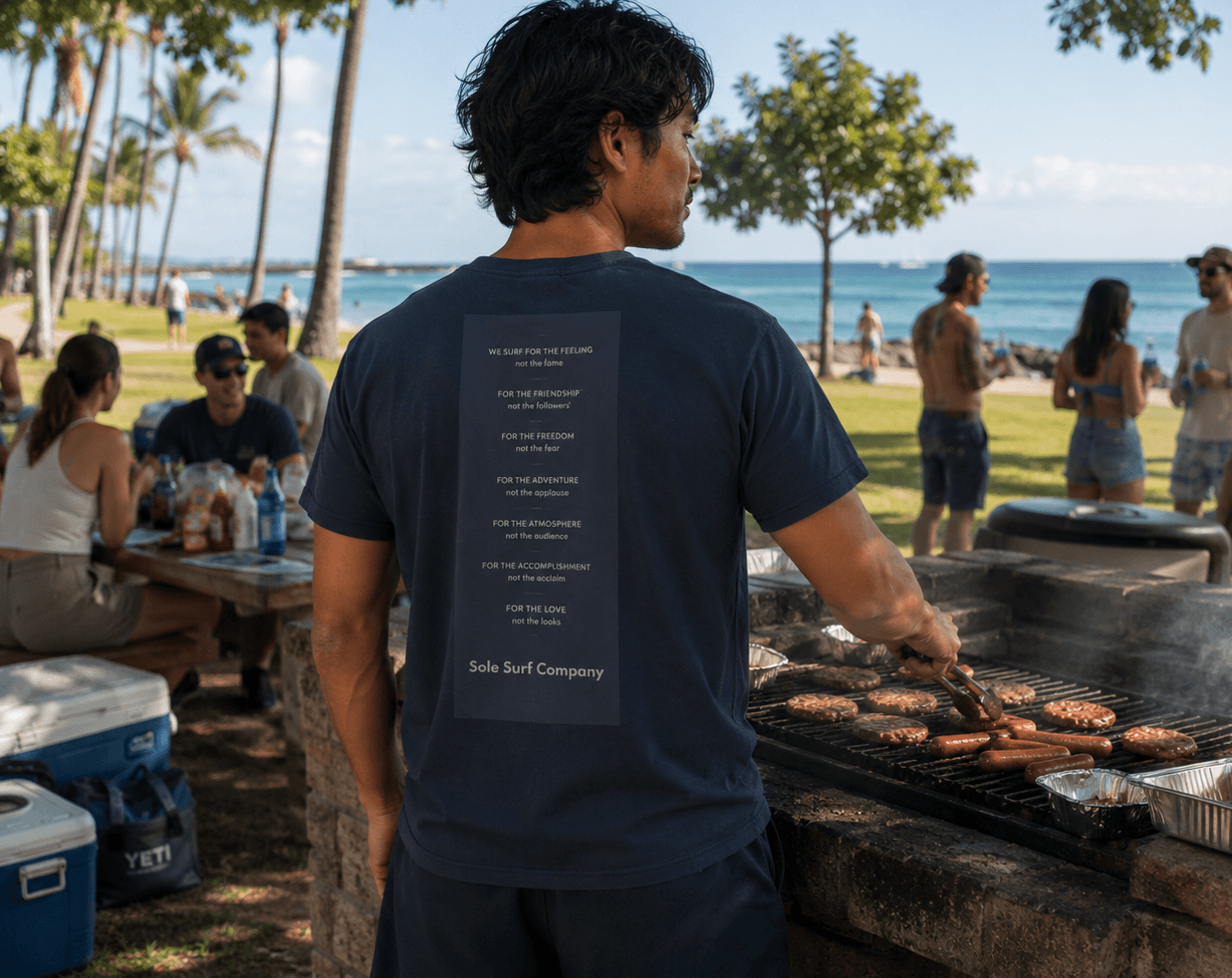 Man grilling at a beachside picnic with people and palm trees in the background