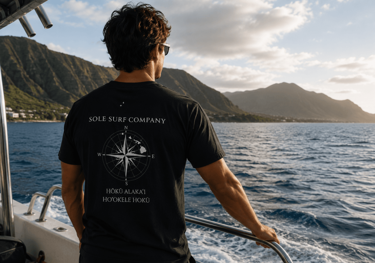 Man on a boat wearing a black t-shirt with 'Sole Surf Company' branding, looking at mountains over water.