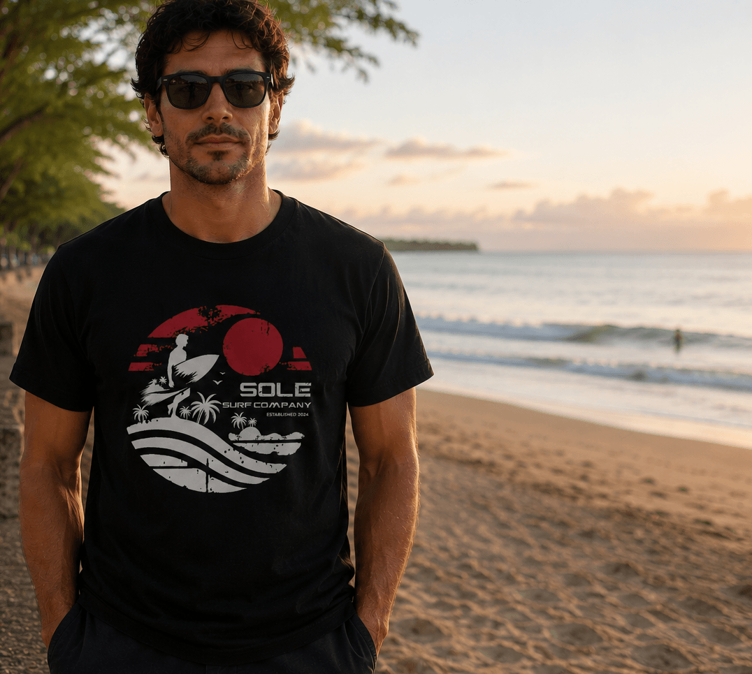 Man wearing a black t-shirt with a graphic design on a beach at sunset