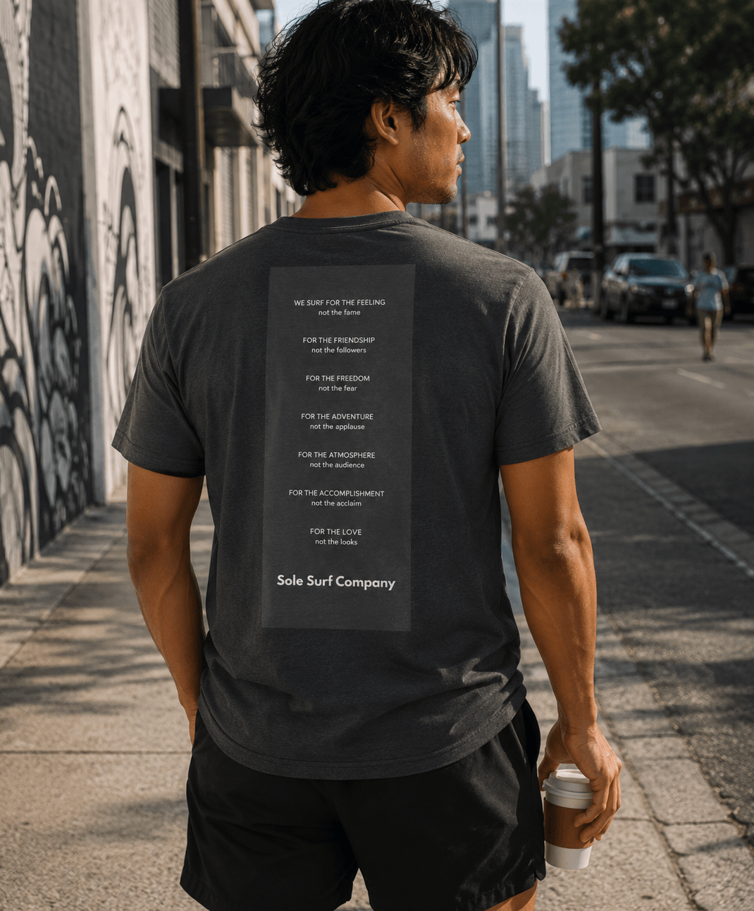 Man walking on a city street wearing a gray t-shirt with text on the back.
