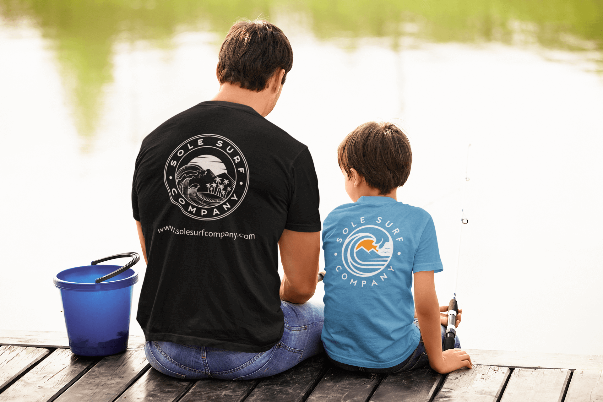 Father and son fishing together, wearing Sole Surf Company t-shirts by a serene lake.