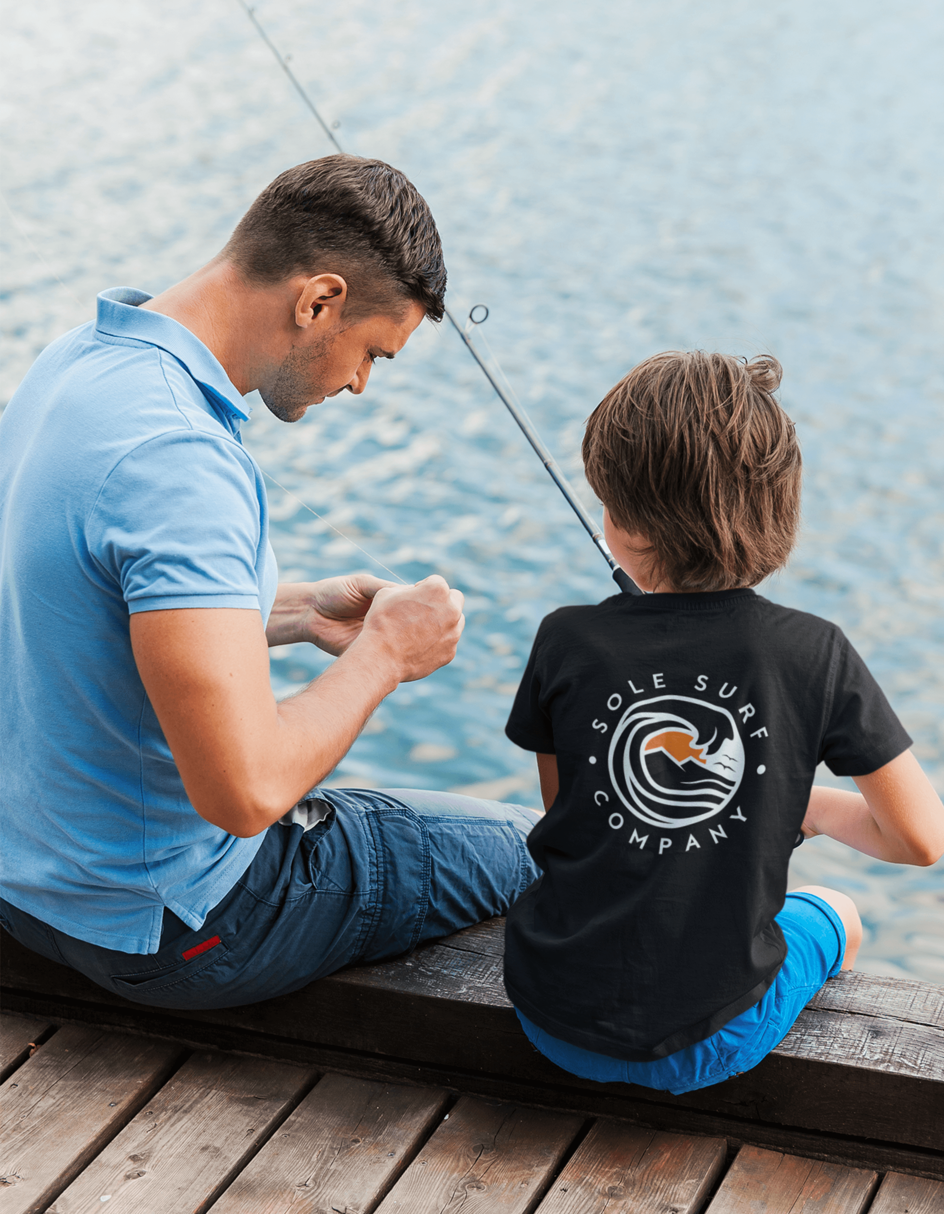 Father and son fishing by the water, showcasing the kids' logo tee from Sole Surf Company.